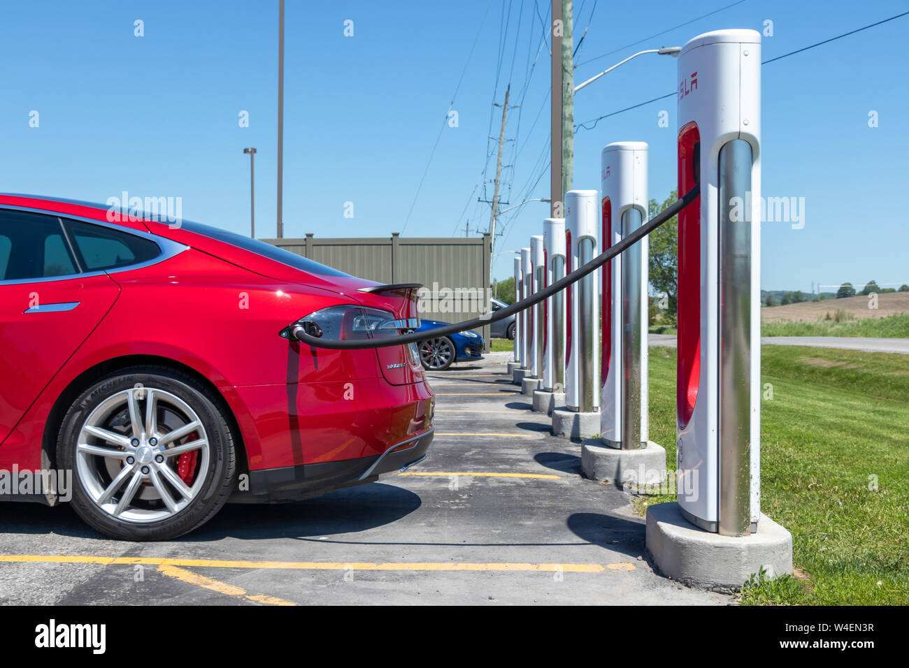 Metallic Red Tesla Model S plugged-in, charging at Tesla Supercharger Station. Stock Photo
