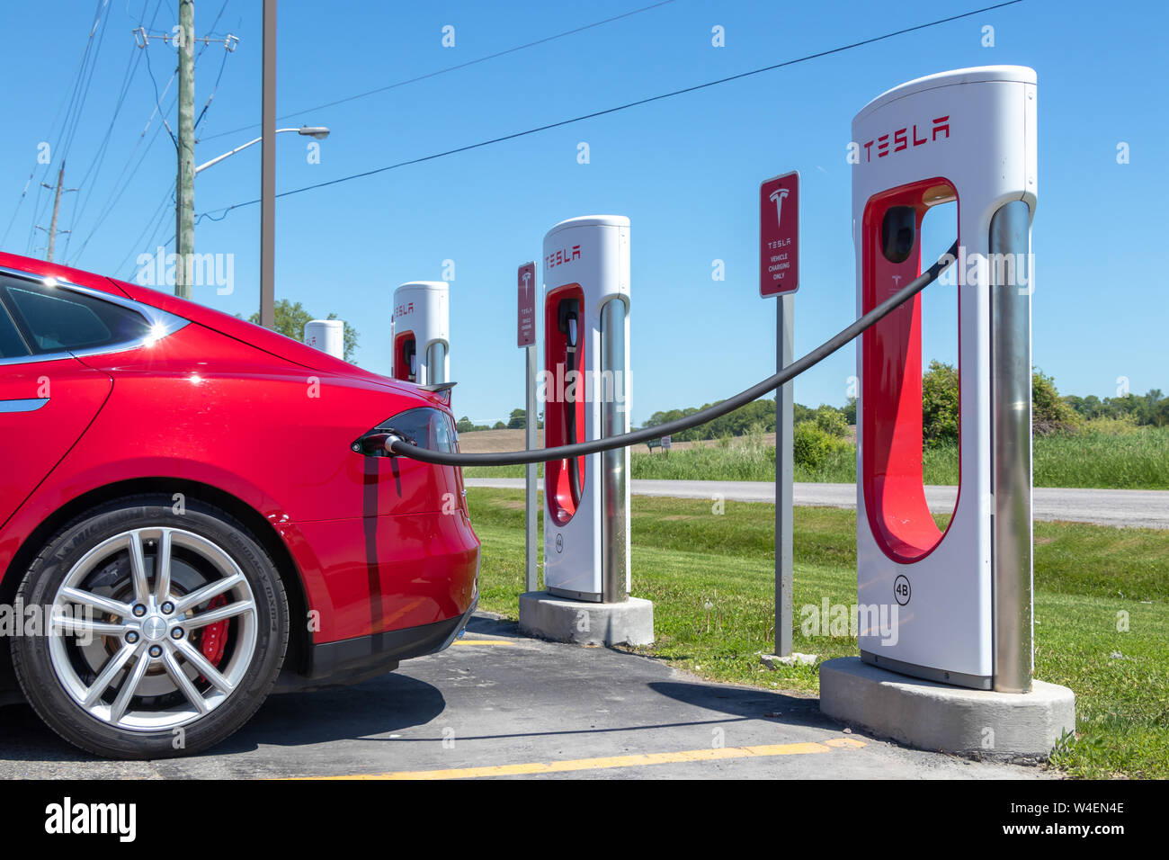 Metallic Red Tesla Model S plugged-in, charging at Tesla Supercharger Station in Port Hope, Ontario. Stock Photo