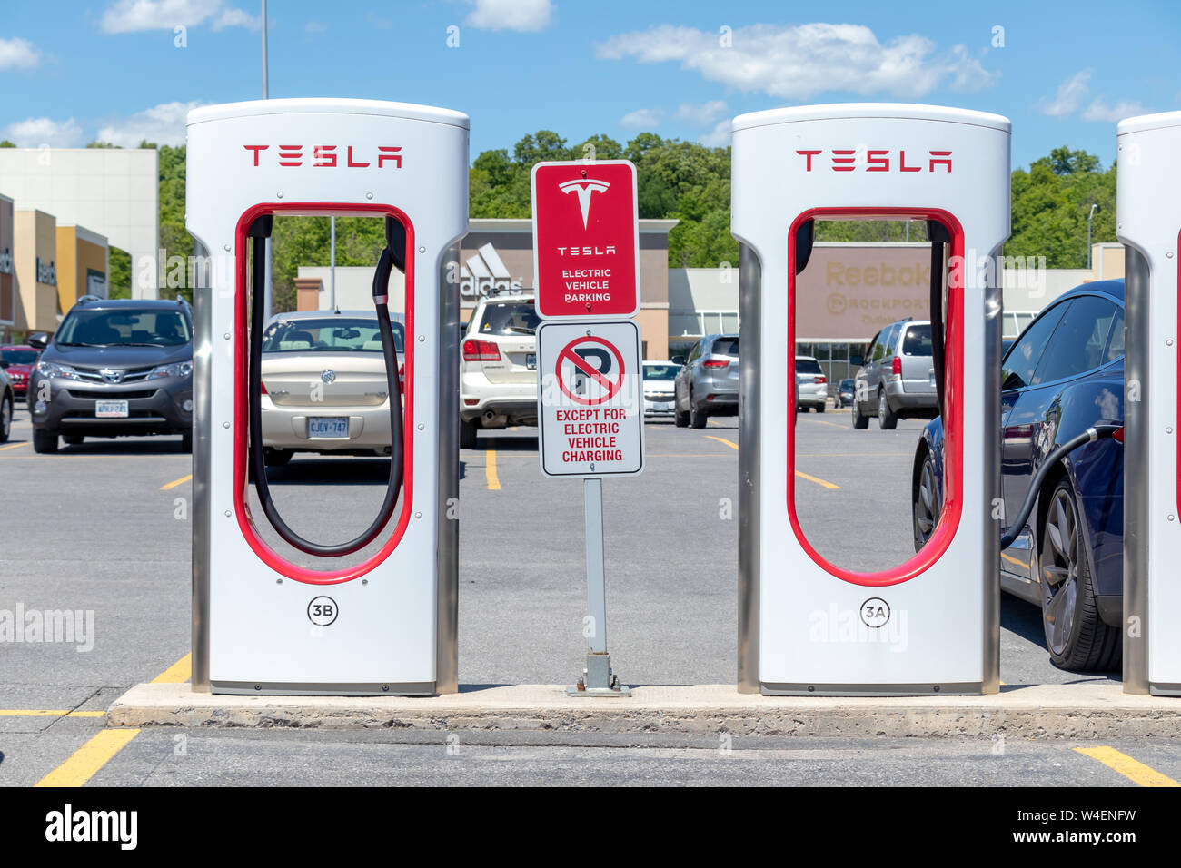 Tesla Supercharger Stalls in Kingston, Ontario with parking restriction signs and blue Tesla Model S charging in the background. Stock Photo