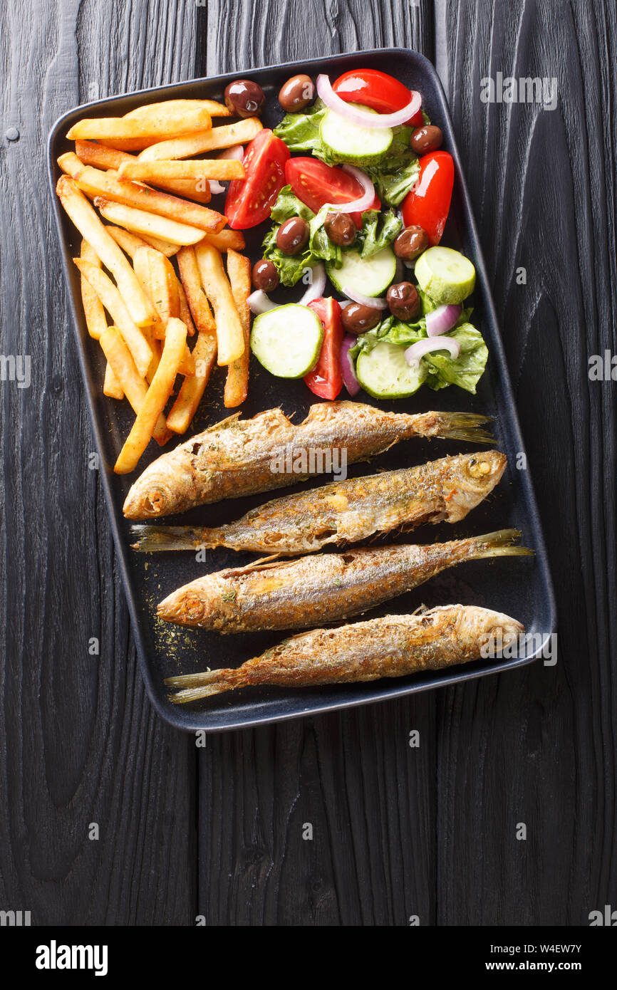Fresh fried boops boops fish with summer vegetable salad and french fries close-up on a plate on the table. Vertical top view from above Stock Photo