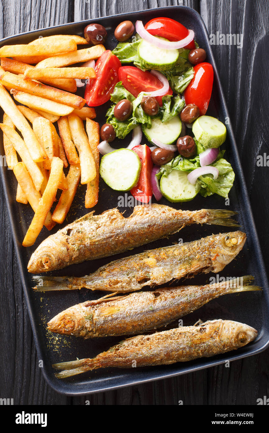 Fried Mediterranean Boops boops fish served with fresh salad and french fries close-up on a plate on the table. Vertical top view from above Stock Photo