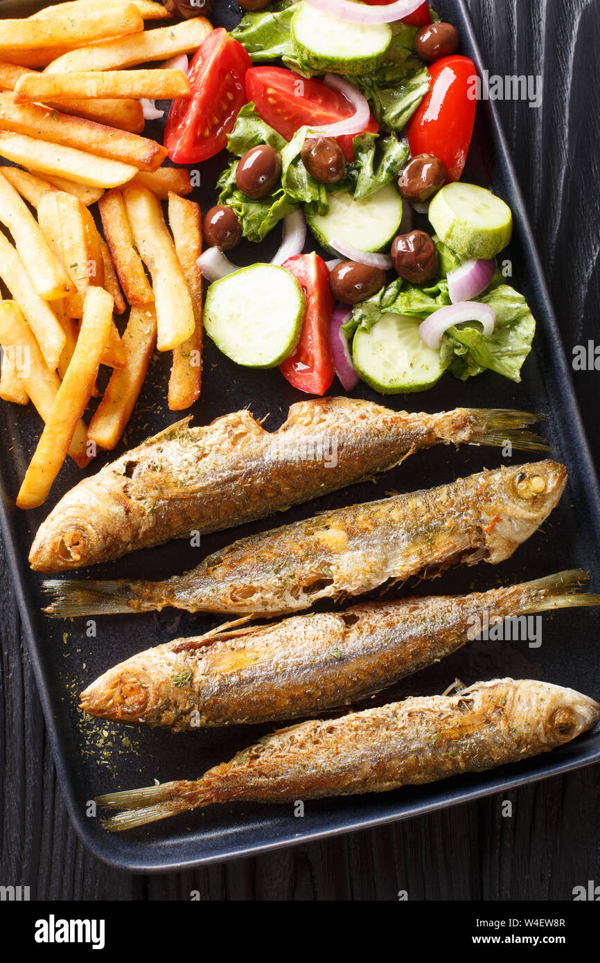 Fried boops boops fish with fresh vegetable salad and french fries close-up on a plate on the table. Vertical top view from above Stock Photo
