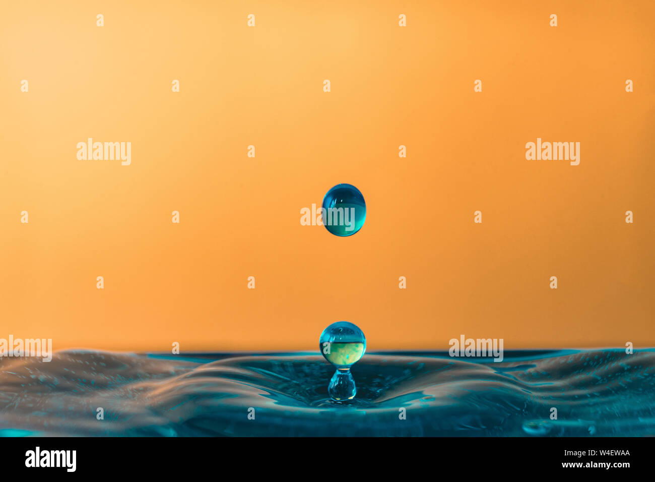 Drop of water, blue water drop, water splash closeup isolated on orange background, a lot of