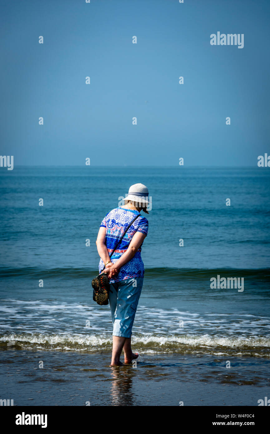 Woman walking along a sandy beach with blue sea and sky Stock Photo