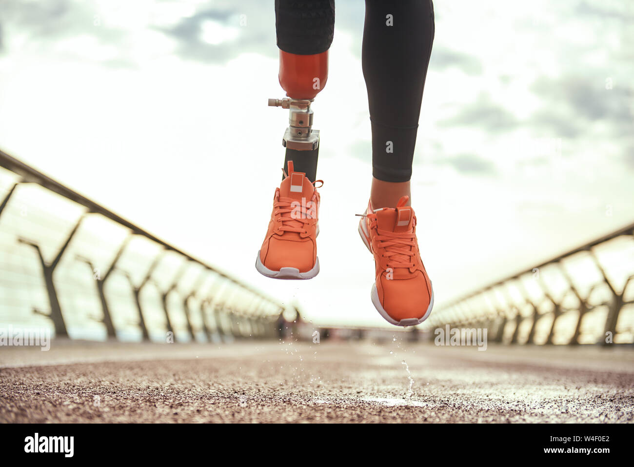 Never give up Cropped photo of disabled woman with prosthetic leg in sportswear jumping on the bridge. Disabled sport concept. Motivation Stock Photo