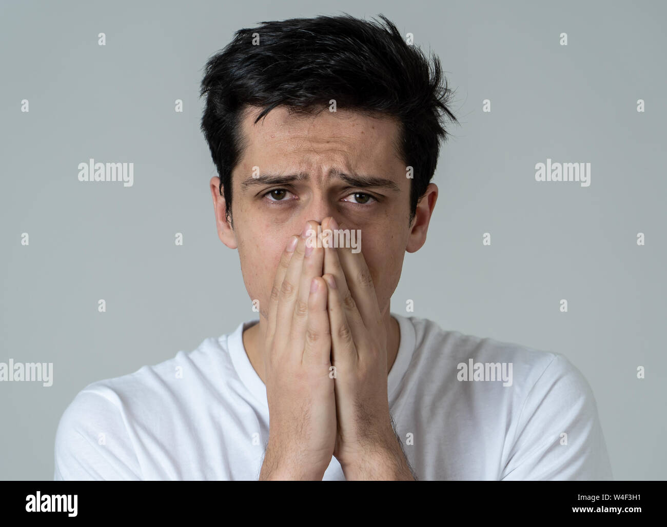 Close up of a young sad man, serious and concerned, looking worried and thoughtful. Covering her mouth like sneezing, feeling feverish and cold. With Stock Photo