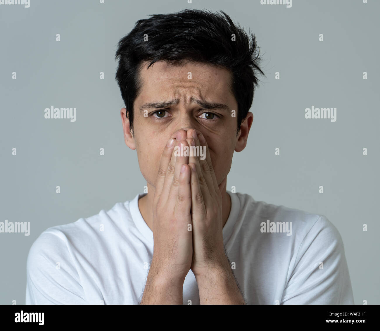 Close up of a young sad man, serious and concerned, looking worried and thoughtful. Covering her mouth like sneezing, feeling feverish and cold. With Stock Photo