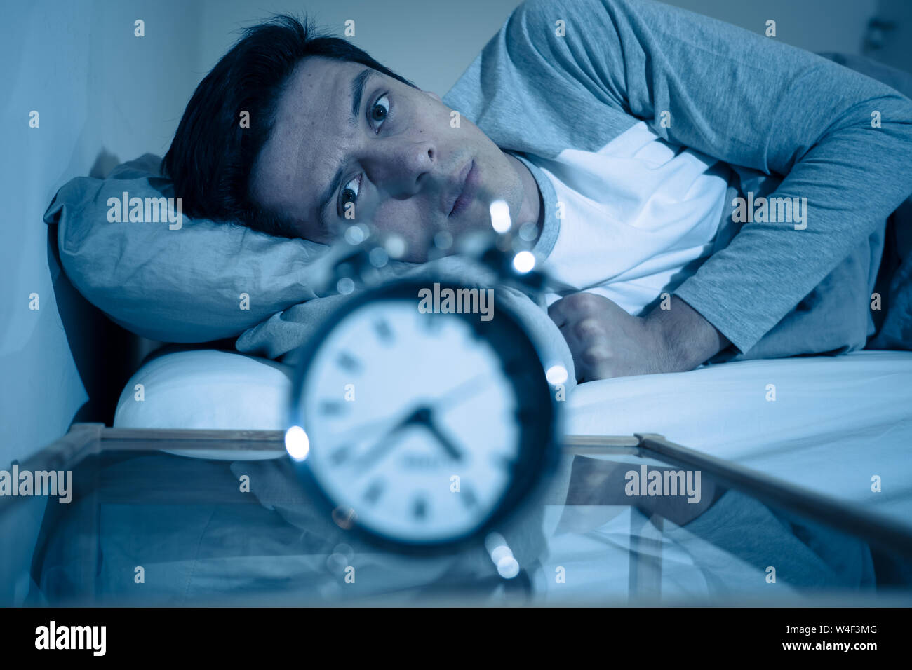 Sleepless and desperate young caucasian man awake at night not able to sleep, feeling frustrated and worried looking at clock suffering from insomnia Stock Photo