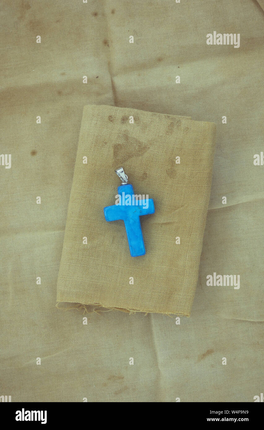 Small bright blue stone crucifix with chain loop lying on stained and folded linen Stock Photo