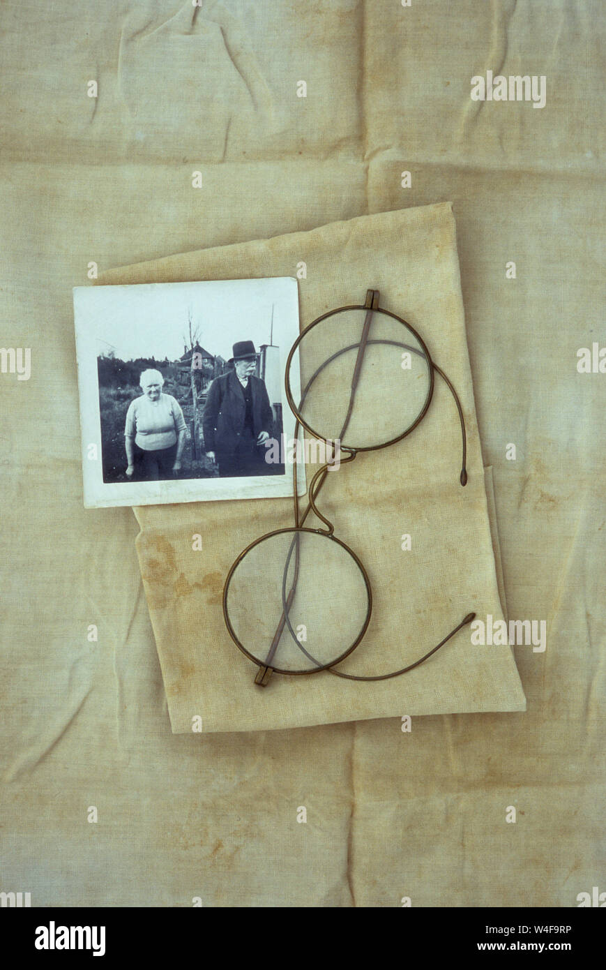 Antique spectacles with circular lenses and wire frames lying on stained and folded linen with black and white photo of elderly 1930s couple Stock Photo