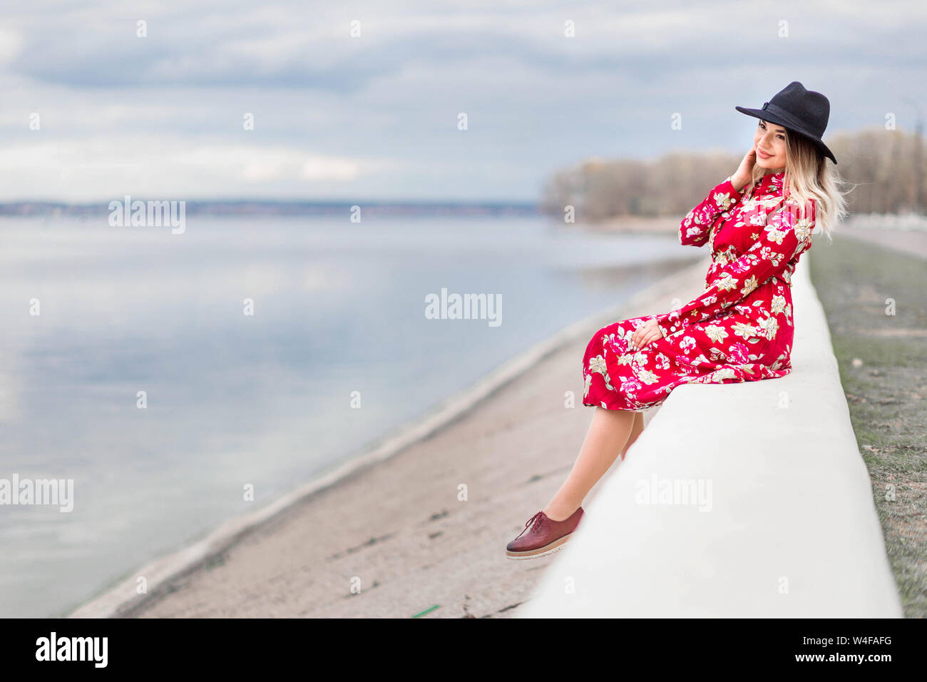Photo of Beautiful girl in a red dress and black hat sits on the ...
