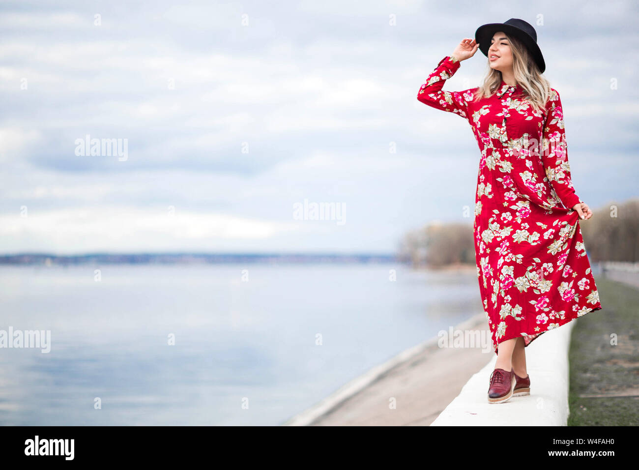 Photo of Beautiful girl in a red dress and black hat stands on the ...