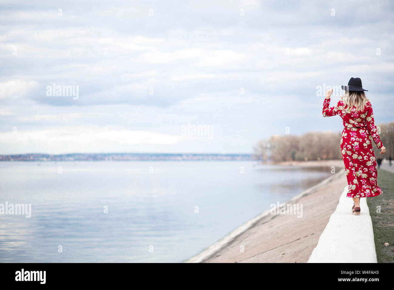 Photo of Beautiful girl in a red dress and black hat stands on the ...