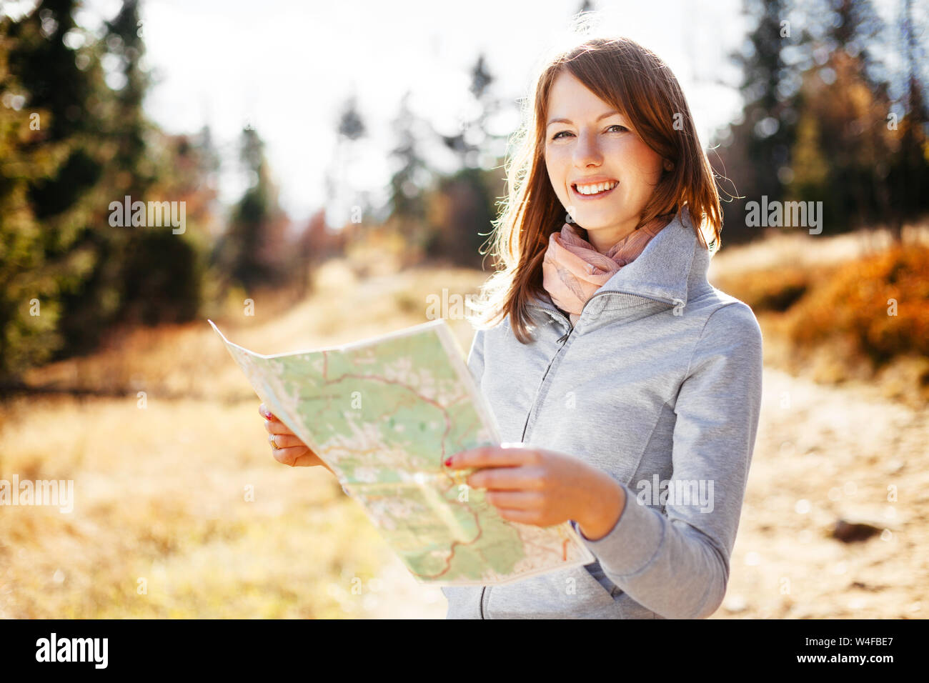 Happy woman reading map on trial during autumn in mountains Stock Photo