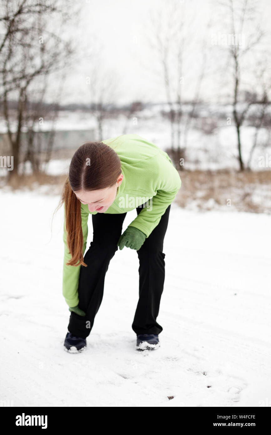 Woman holding leg in pain while jogging outdoors on snowy winter day Stock Photo