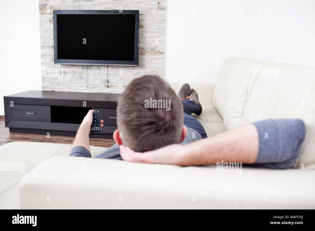 Single man on the couch watching tv, changing channels Stock Photo