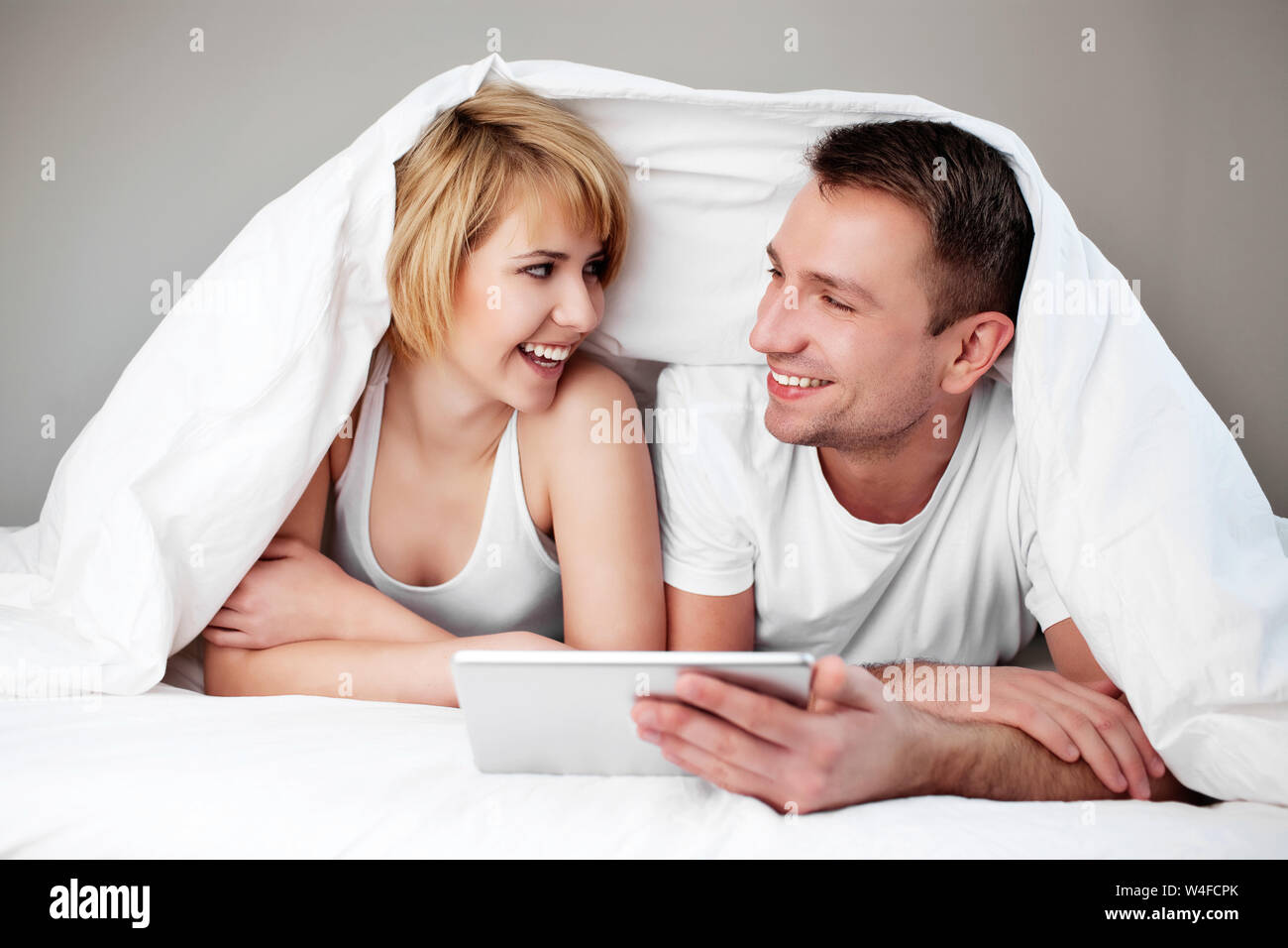Happy couple lying in bed with digital tablet Stock Photo