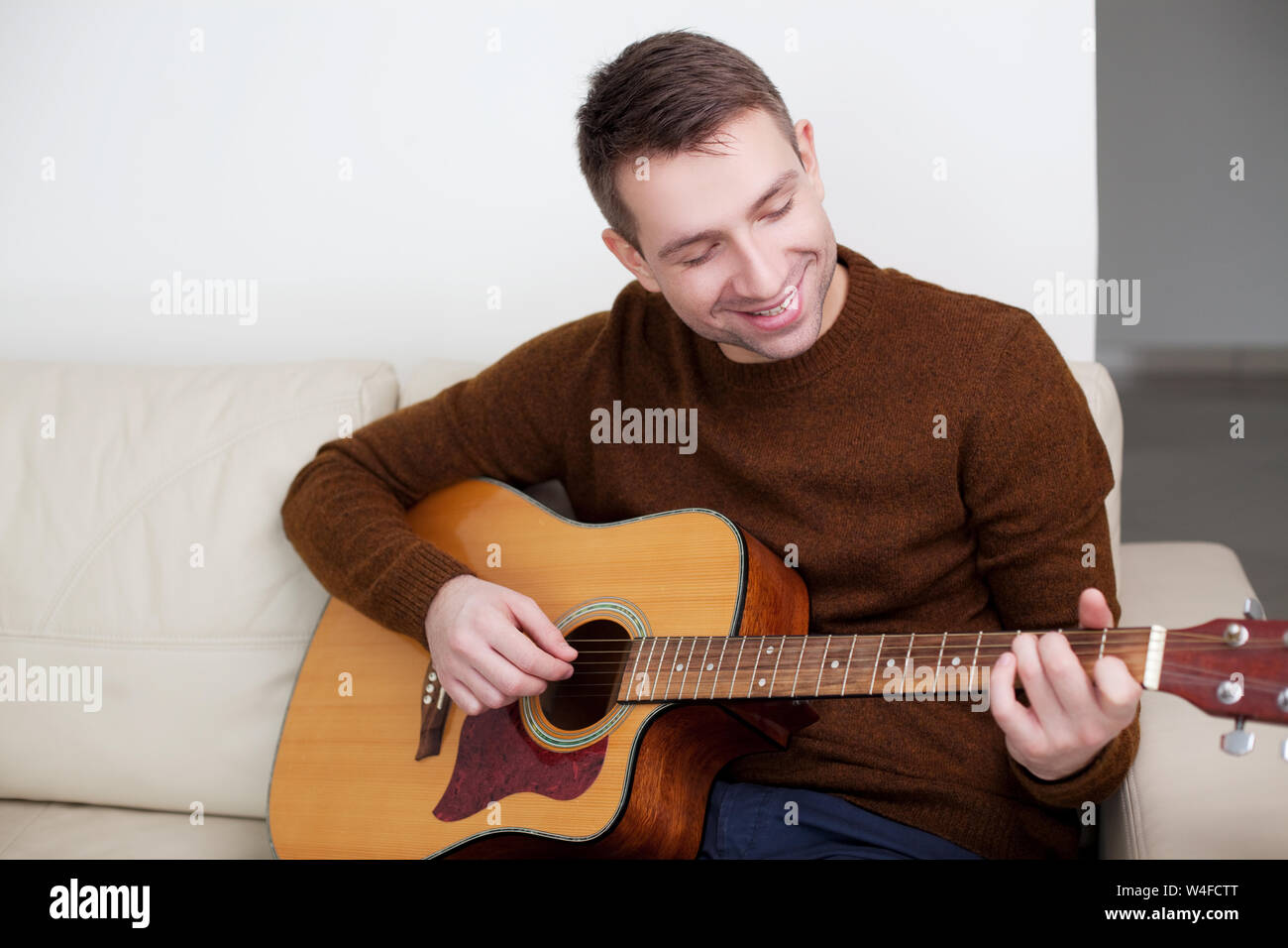 Handsome young man playing guitar, sitting on sofa Stock Photo