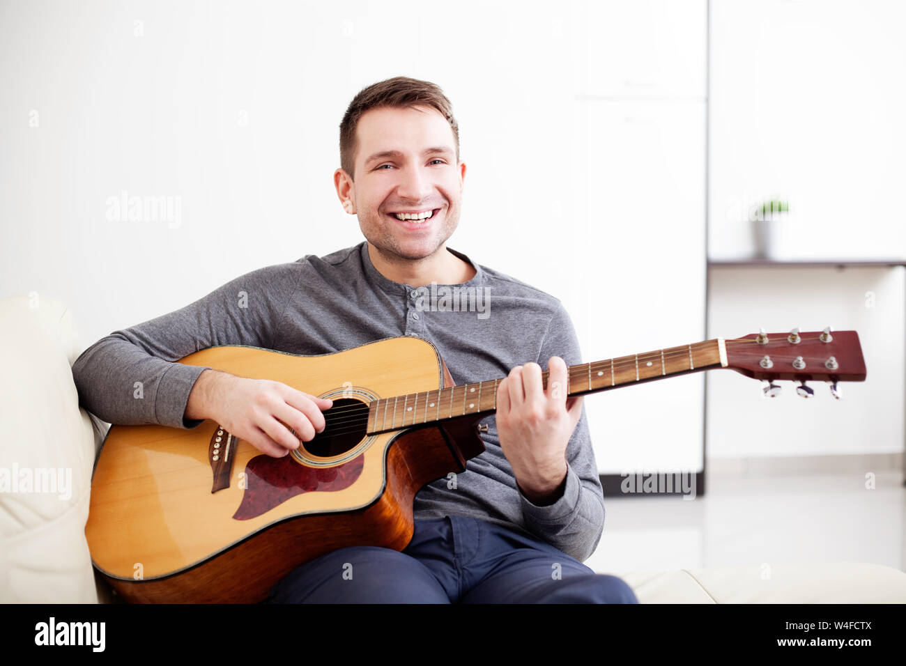 Handsome young man playing guitar, sitting on sofa Stock Photo