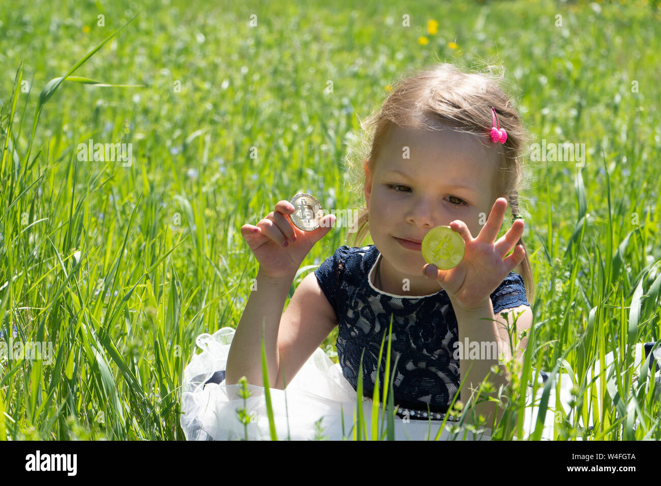 Little girl holding a bitcoin cryptocurrency coin in hands. A child plays  with gold coins sitting on the grass Stock Photo - Alamy
