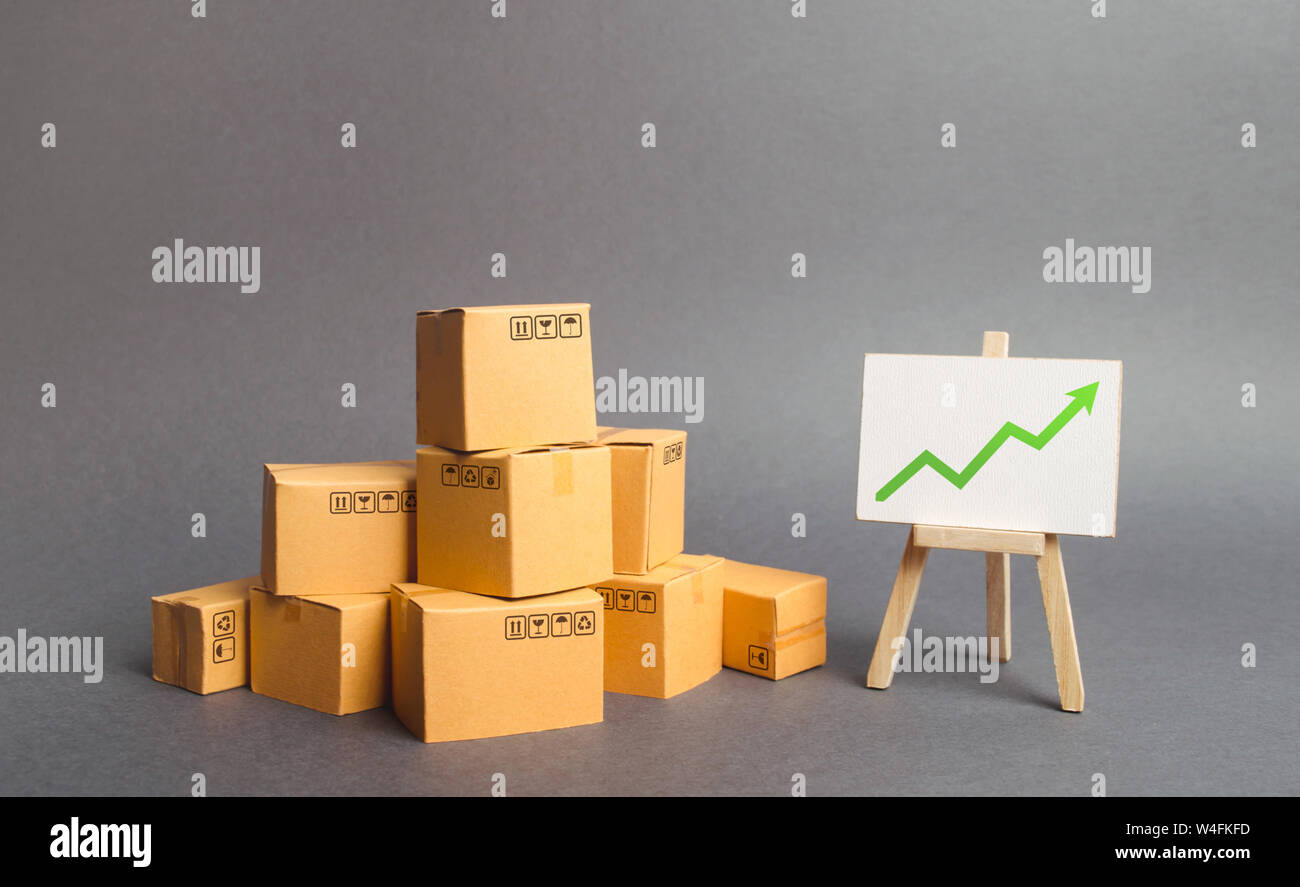 Plenty of cardboard boxes and whiteboard with green positive chart arrow up. Increasing consumer demand. rate growth of production of goods and produc Stock Photo