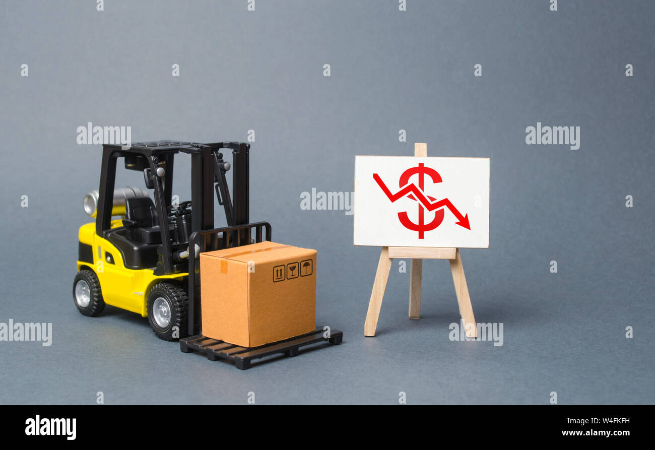 Forklift truck carries a cardboard box near a stand with a red dollar arrow down. decline in the production of goods and products, economic downturn a Stock Photo