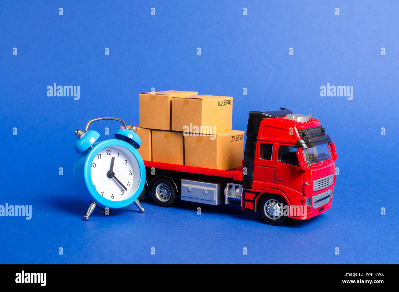 A red truck with cardboard boxes and a blue alarm clock. Express delivery in short time concept. Temporary storage, limited offer and discount. Optimi Stock Photo
