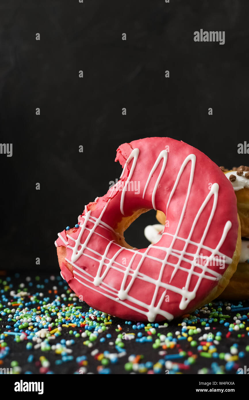 Pink frosted donut with bite missing over black background. Stack of doughnuts. Copy space. Stock Photo