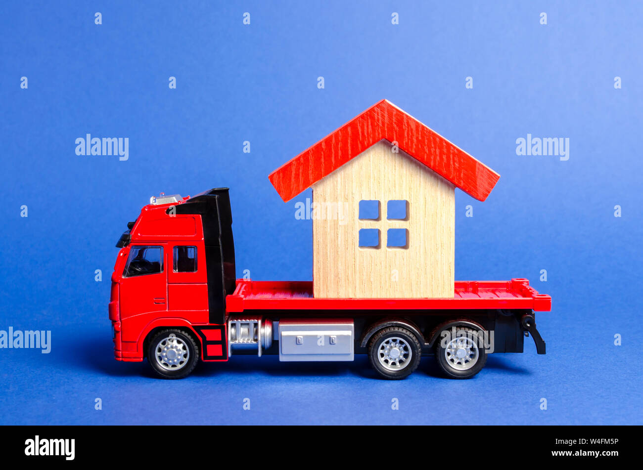 Red truck transports a red roofed house. Concept of transportation and cargo shipping, moving company. Construction of new houses and objects. Industr Stock Photo