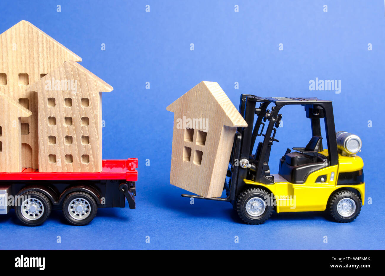 A yellow forklift loads a wooden figure of a house into a truck. Concept of transportation and cargo shipping, moving company. Construction of new hou Stock Photo