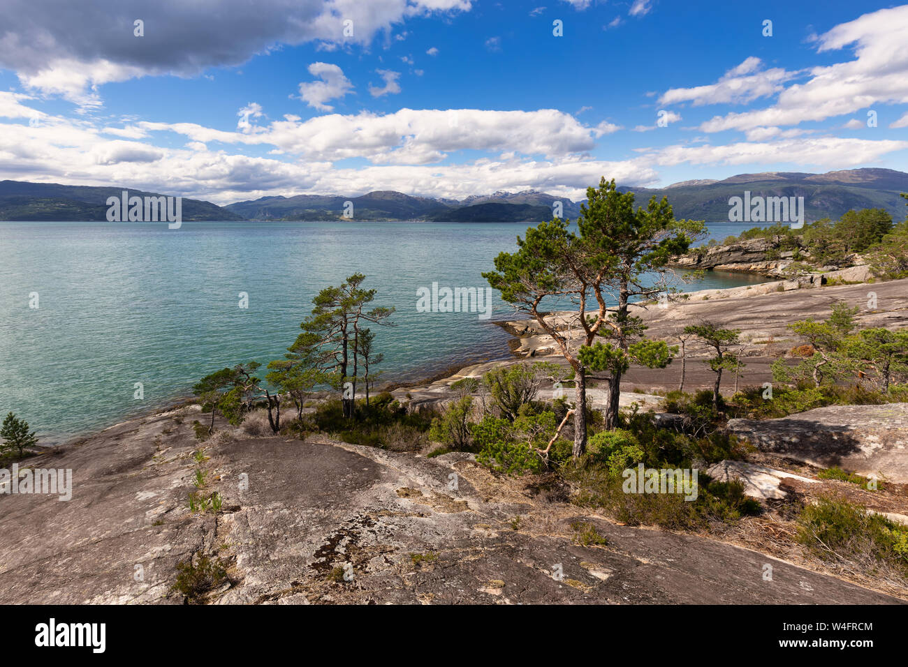A wilderness landscape in Norway at the Geiranger Fjord in summer with a blue sky and white clouds and rocks in foreground on a beautiful day. Stock Photo