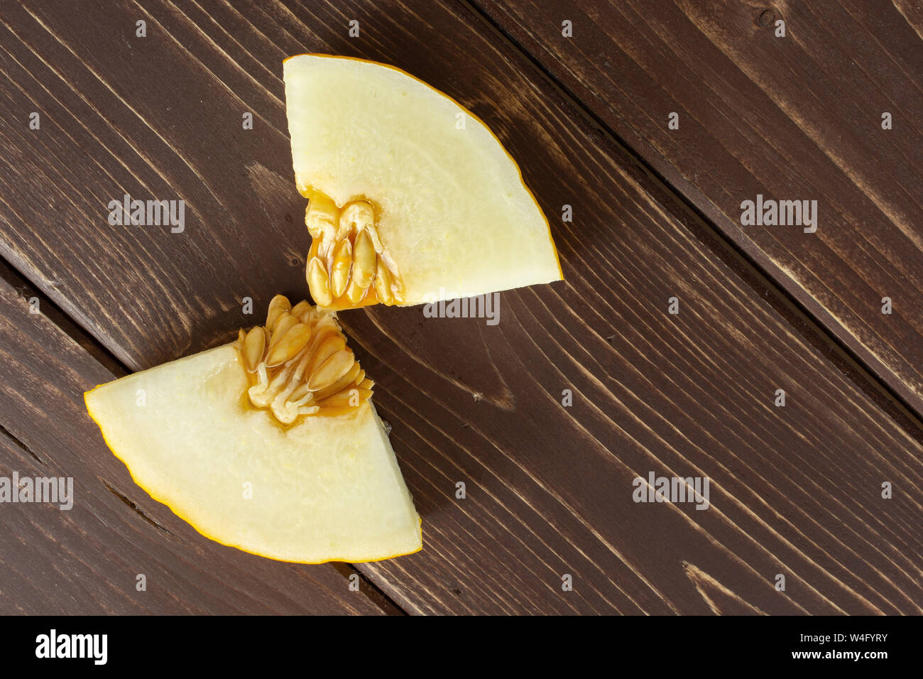 Group of two pieces of fresh yellow melon canary copyspace on right flatlay on brown wood Stock Photo