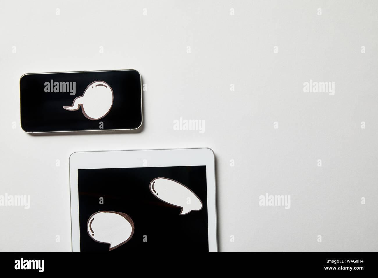 digital tablet and smartphone with paper thought and speech bubbles on white surface Stock Photo