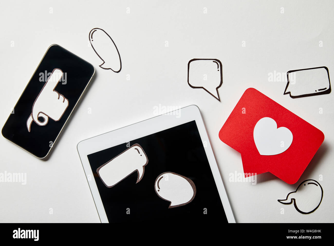 digital tablet and smartphone with paper thought and speech bubbles, paper heart, pointing card on white surface Stock Photo