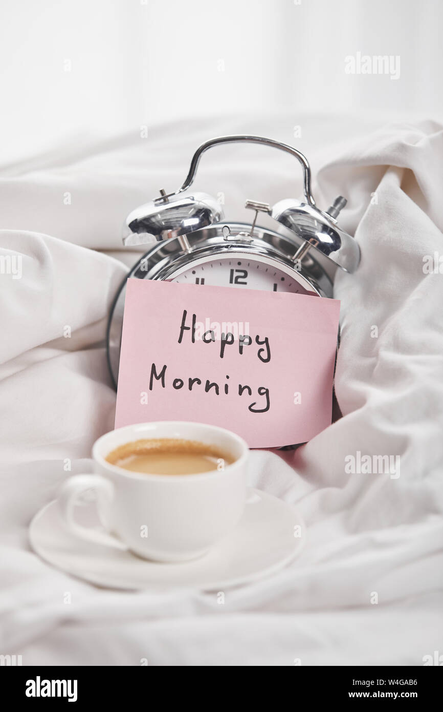 https://c8.alamy.com/comp/W4GAB6/coffee-in-white-cup-on-saucer-near-silver-alarm-clock-with-happy-morning-lettering-on-sticky-note-in-bed-W4GAB6.jpg