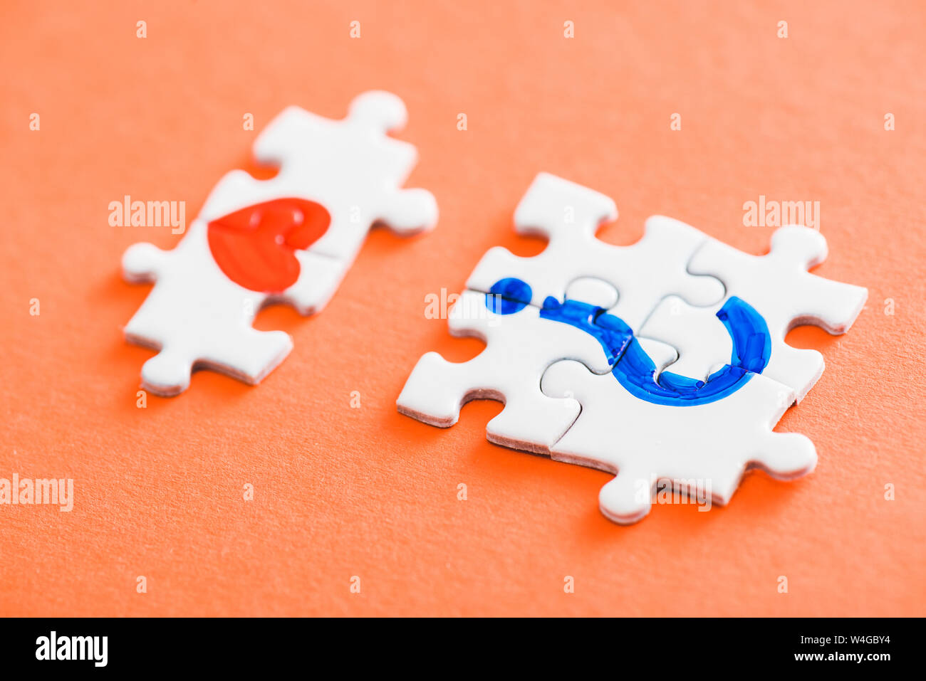 selective focus of connected puzzle pieces with drawn red heart and blue question mark on orange Stock Photo