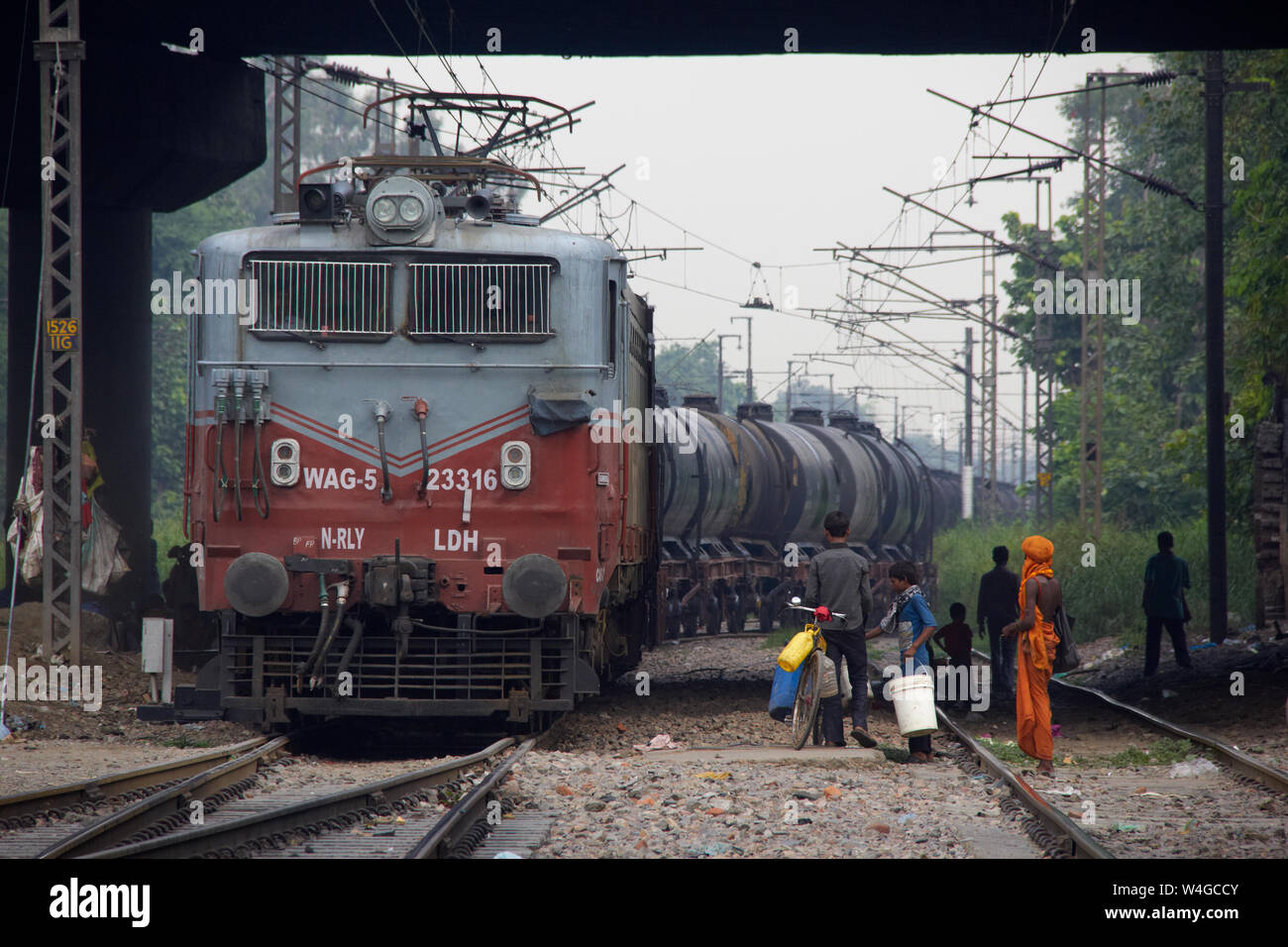 Freight train running on track and a group of people waiting to cross