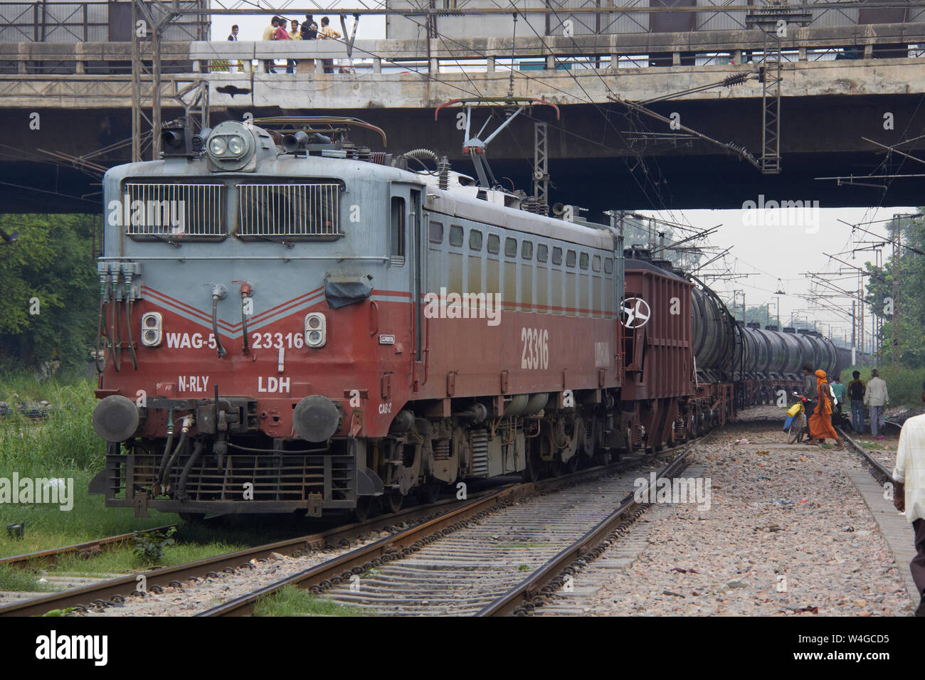 Freight train running on track and a group of people waiting to cross the track, Delhi, India