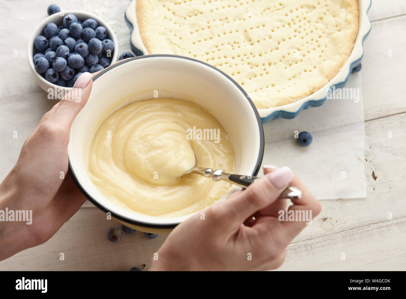 Woman preparing whipped cream for blueberry pie with fresh berries. Blueberry tart cooking recipe. Stock Photo