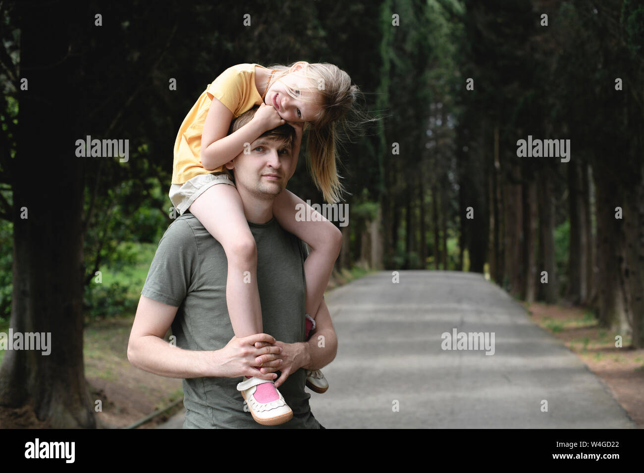 Father carrying daughter on a treelined road Stock Photo