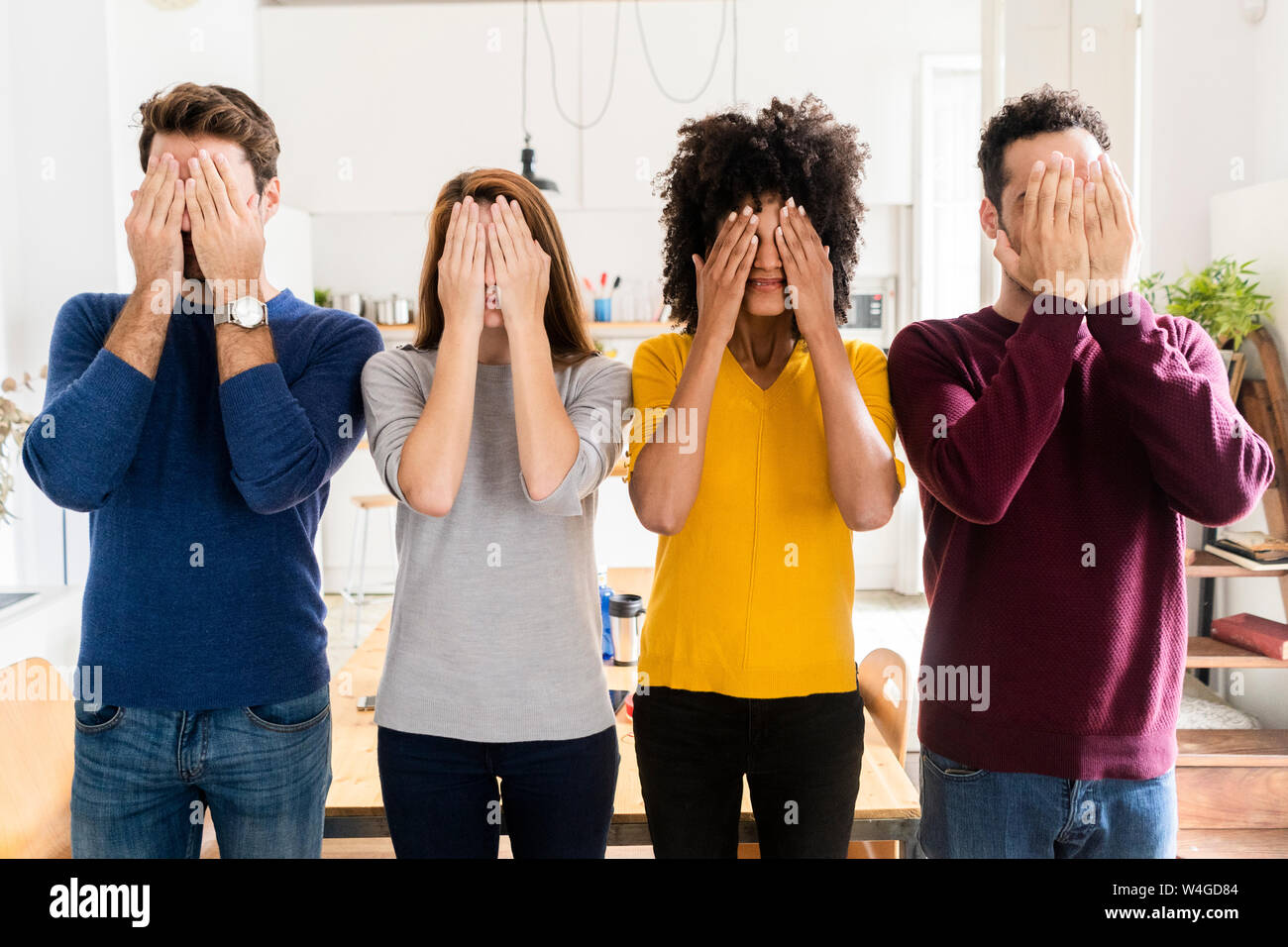 Four friends standing side by side at home covering their faces Stock Photo