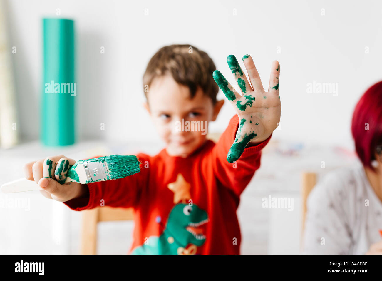 Boy showing a brush in one hand and the other painted green while doing crafts at home Stock Photo