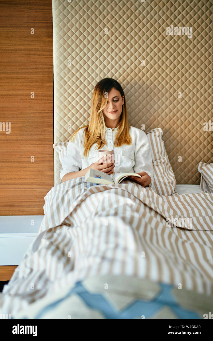 Woman sitting in bed, reading a book Stock Photo