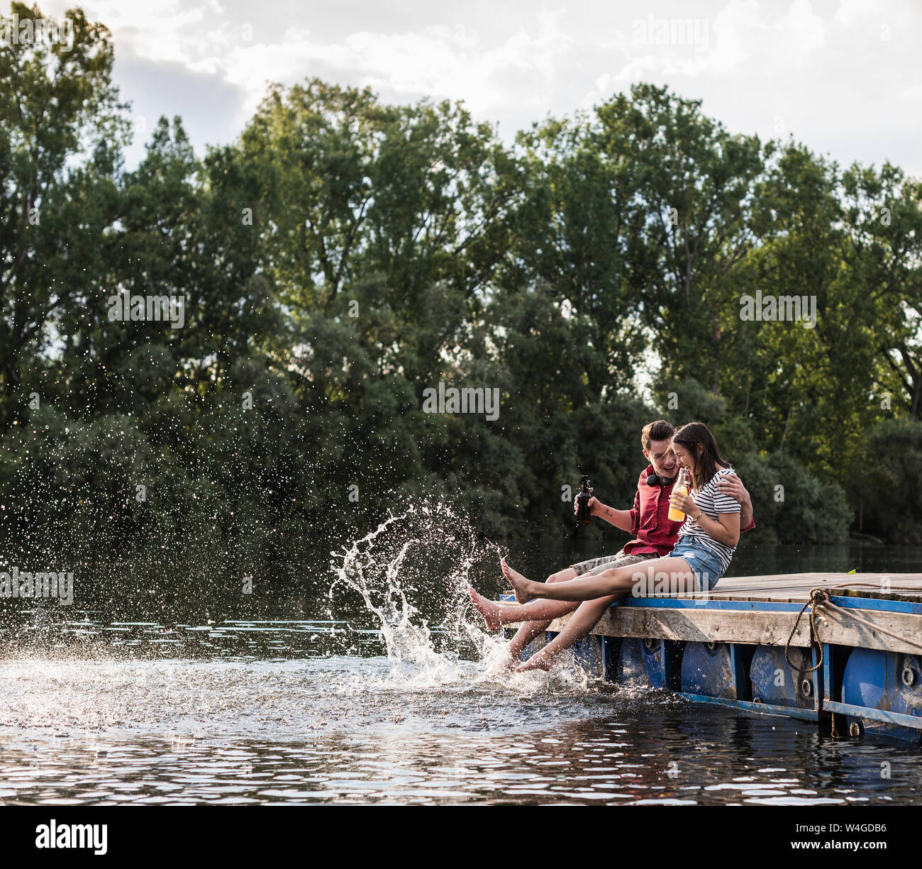 Young couple having a drink and splashing with water on jetty at a remote lake Stock Photo