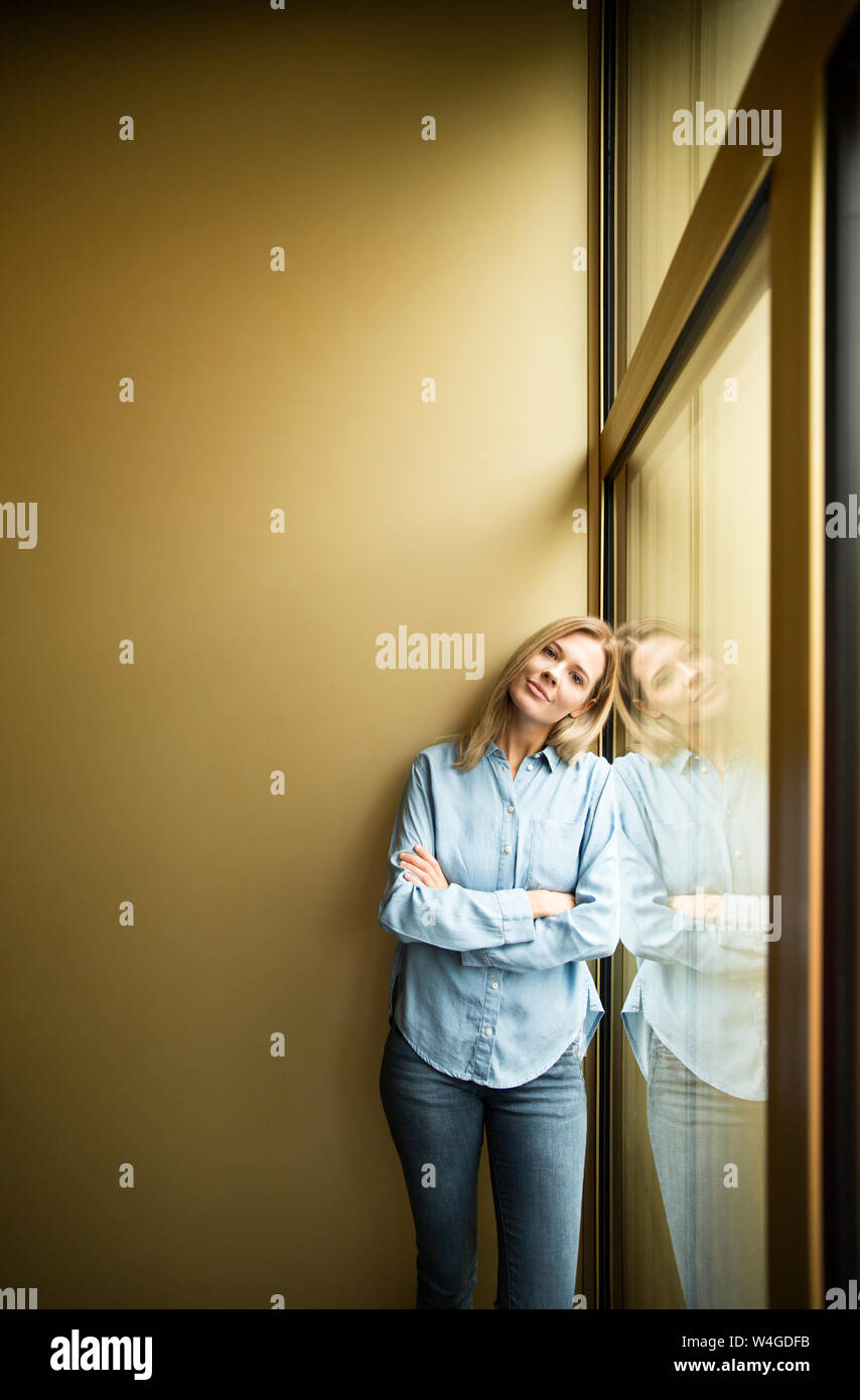 Businesswoman standing on a window, looking on camera, ams crossed Stock Photo