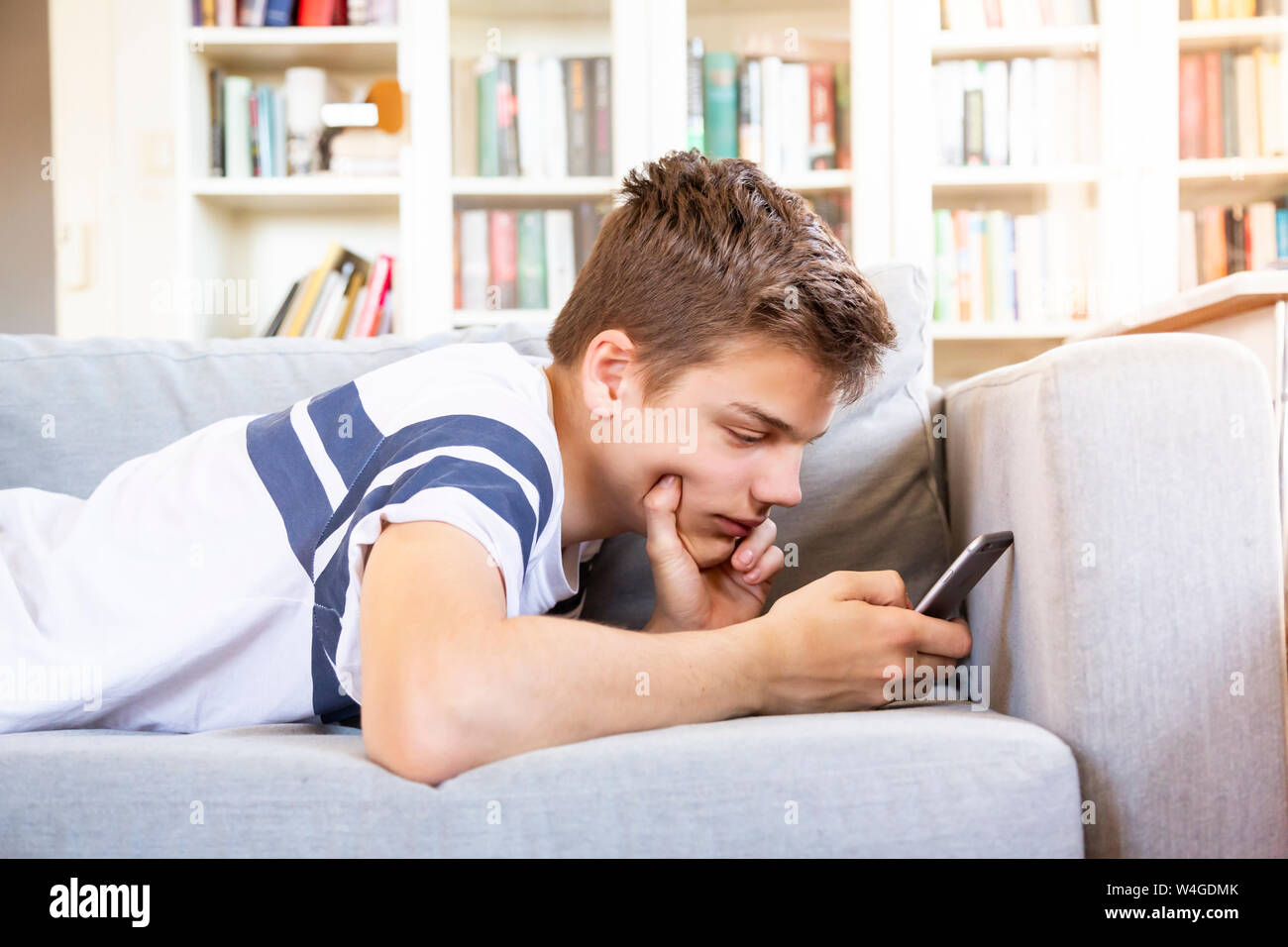 Teenage boy lying on the couch at home using cell phone Stock Photo