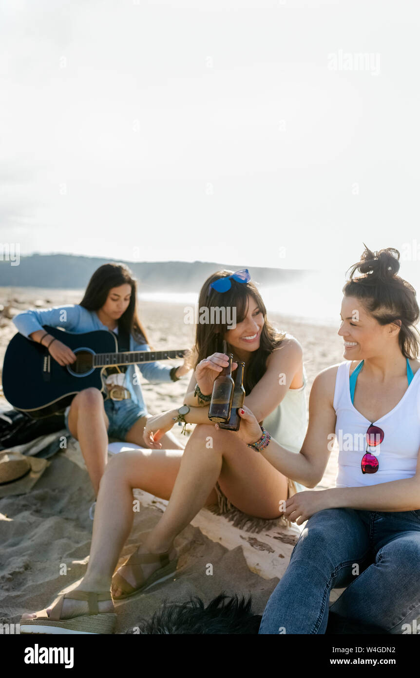 Young woman with friends playing guitar on the beach Stock Photo