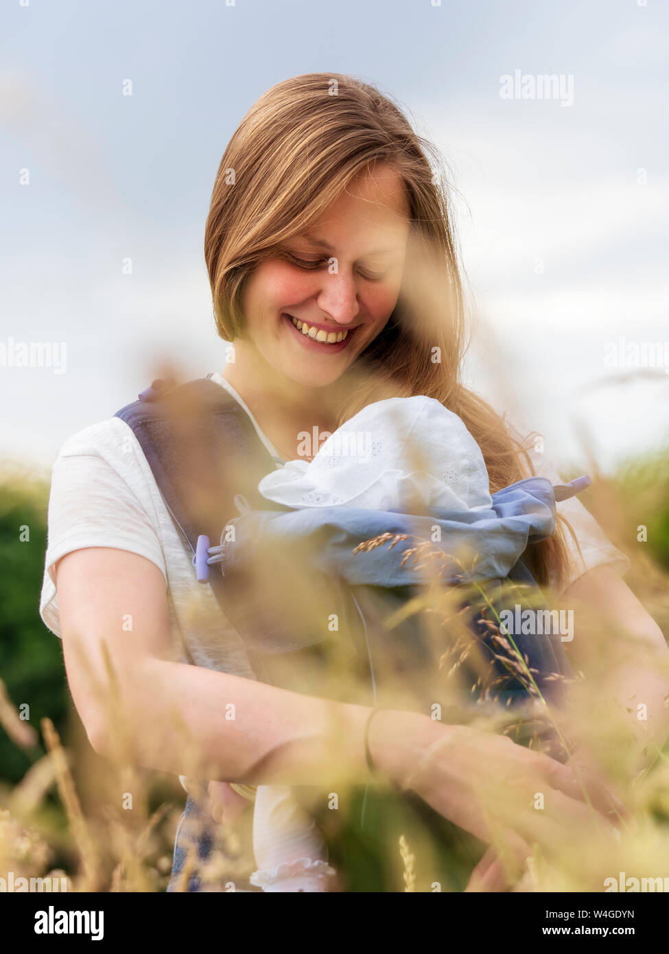 Portrait of happy mother carrying her little daughter in baby sling in nature Stock Photo