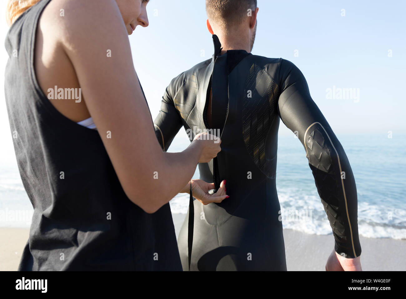 Woman zipping up man's wetsuit at the beach Stock Photo