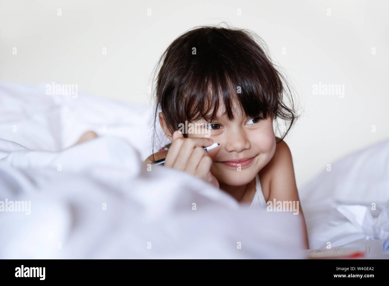 Portrait of smiling little girl lying in bed with felt tip pen Stock